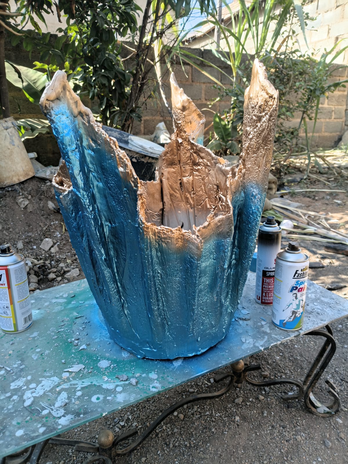 Flower pot being spray-painted in progress with teal and gold paint